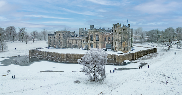 Raby Castle and surrounding park covered in snow with people walking in grounds.